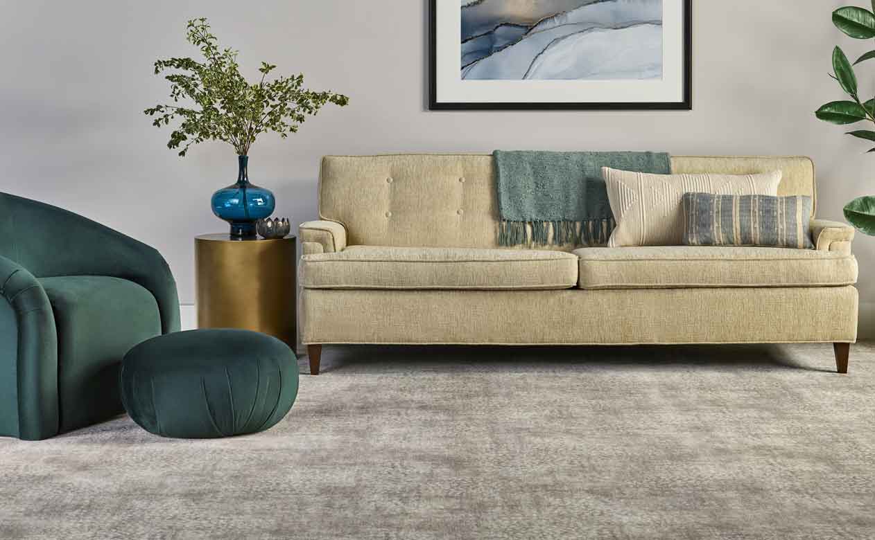 living room with green velvet chair, ottoman and beige couch with greige carpeted floor