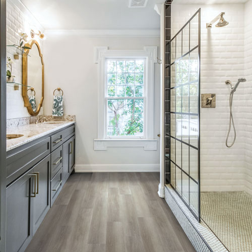 bathroom with gold mirror, tiled shower, and wood look floors